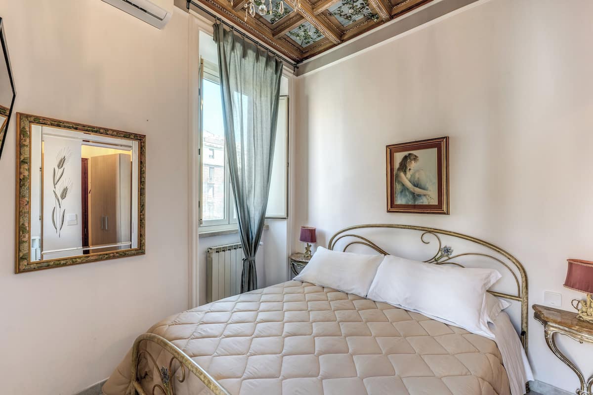A neatly arranged bedroom with a bed, a mirror, a painting, and a nightstand.