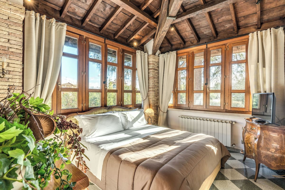 A bedroom with a large bed, wooden ceiling beams, and large windows.
