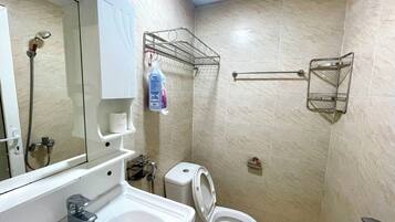 A bathroom with a white sink, toilet, and shower. There are shelves with toiletries and a towel rack.