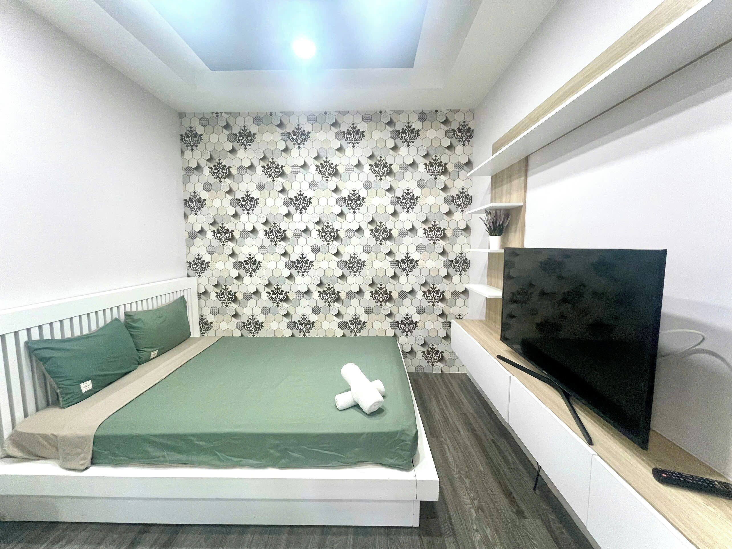 Una camera da letto moderna con un letto, biancheria verde, una televisione e una parete decorata.