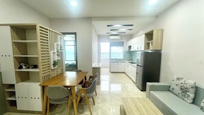 Una cocina moderna con armarios blancos, horno empotrado y refrigerador. Hay un comedor con una mesa y sillas de madera.