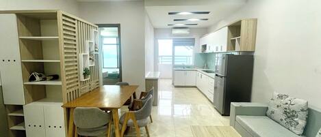 A modern kitchen with white cabinets, a built-in oven, and a refrigerator. There is a dining area with a wooden table and chairs.