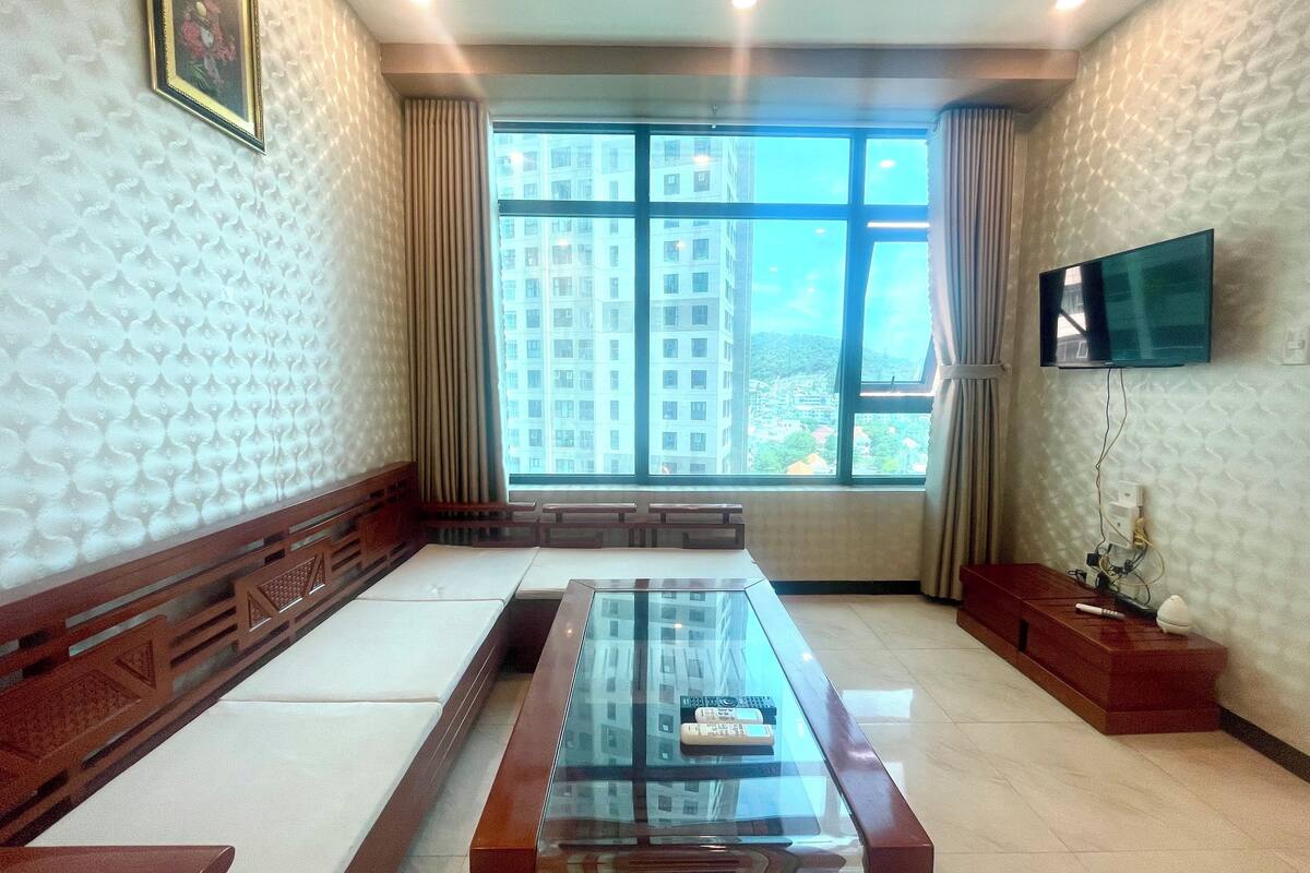 Une chambre d’hôtel moderne dotée d’une grande fenêtre, d’un téléviseur à écran plat fixé au mur et d’une table basse en verre.