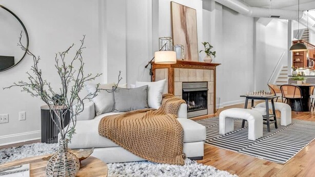 A modern living room with a fireplace, a white sofa, and a dining area with chairs.