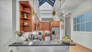 A modern kitchen with a central island, wooden cabinets, and a skylight.