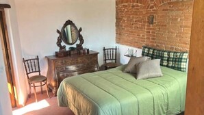 Ein Schlafzimmer mit grüner Bettdecke, einem Holzschrank, einem Spiegel und einer Ziegelwand.