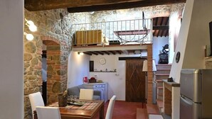 Eine rustikale Küche mit Steinwand, Holzbalken und einem Essbereich mit Tisch und Stühlen.