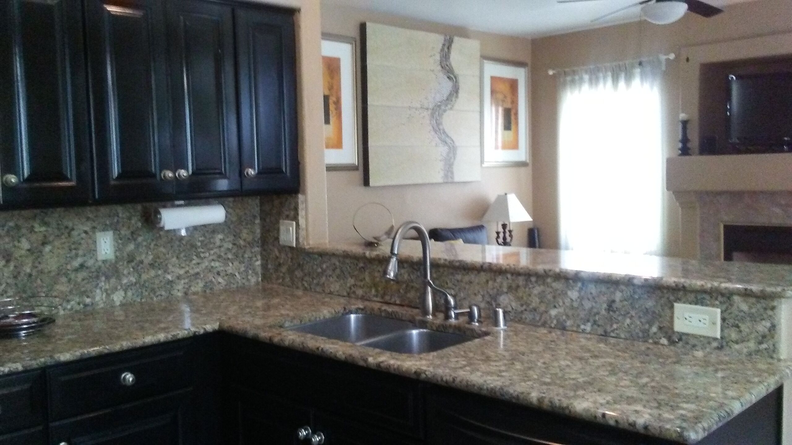 A kitchen with granite countertops, a stainless steel sink, dark cabinets, and a ceiling fan.