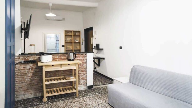 Ein kompakter Wohnbereich mit einer Küchenzeile, einem grauen Sofa und einem Holzbücherregal.