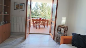 Puerta abierta que da a un balcón con una mesa de comedor y sillas, un armario de madera, y una mesita con lámpara.