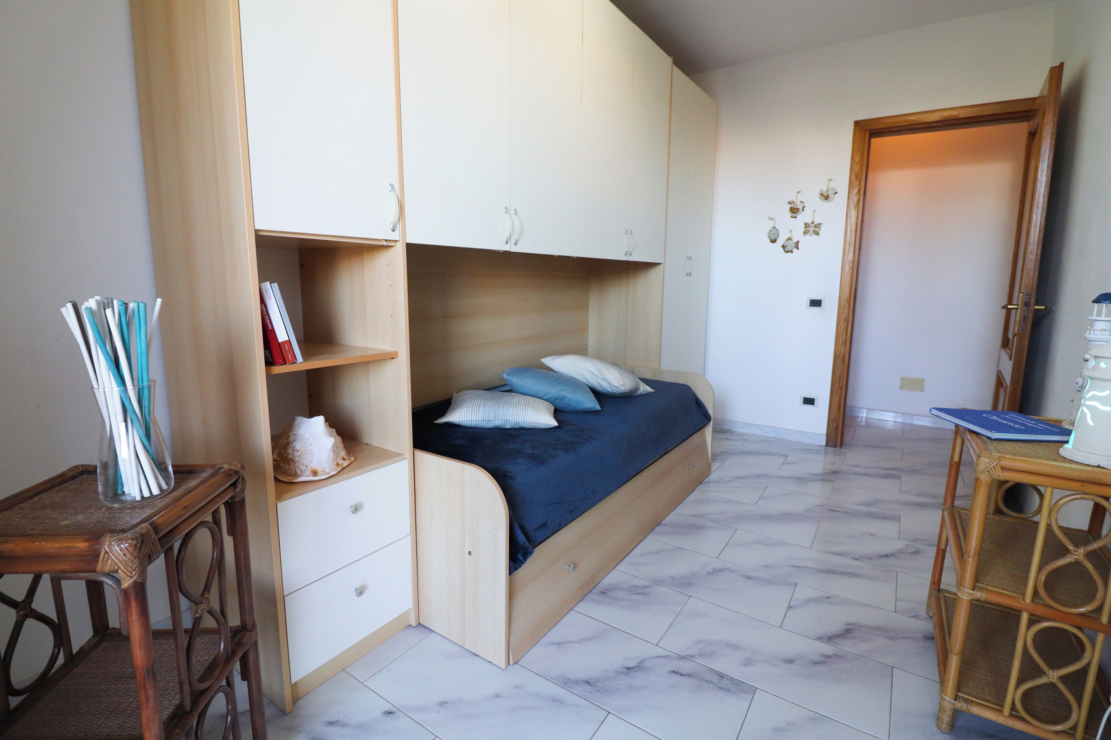 Un dormitorio con cama, armario de madera y una mesita con libros.