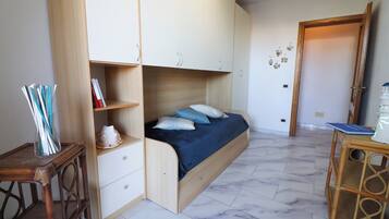 Un dormitorio con cama, armario de madera y una mesita con libros.