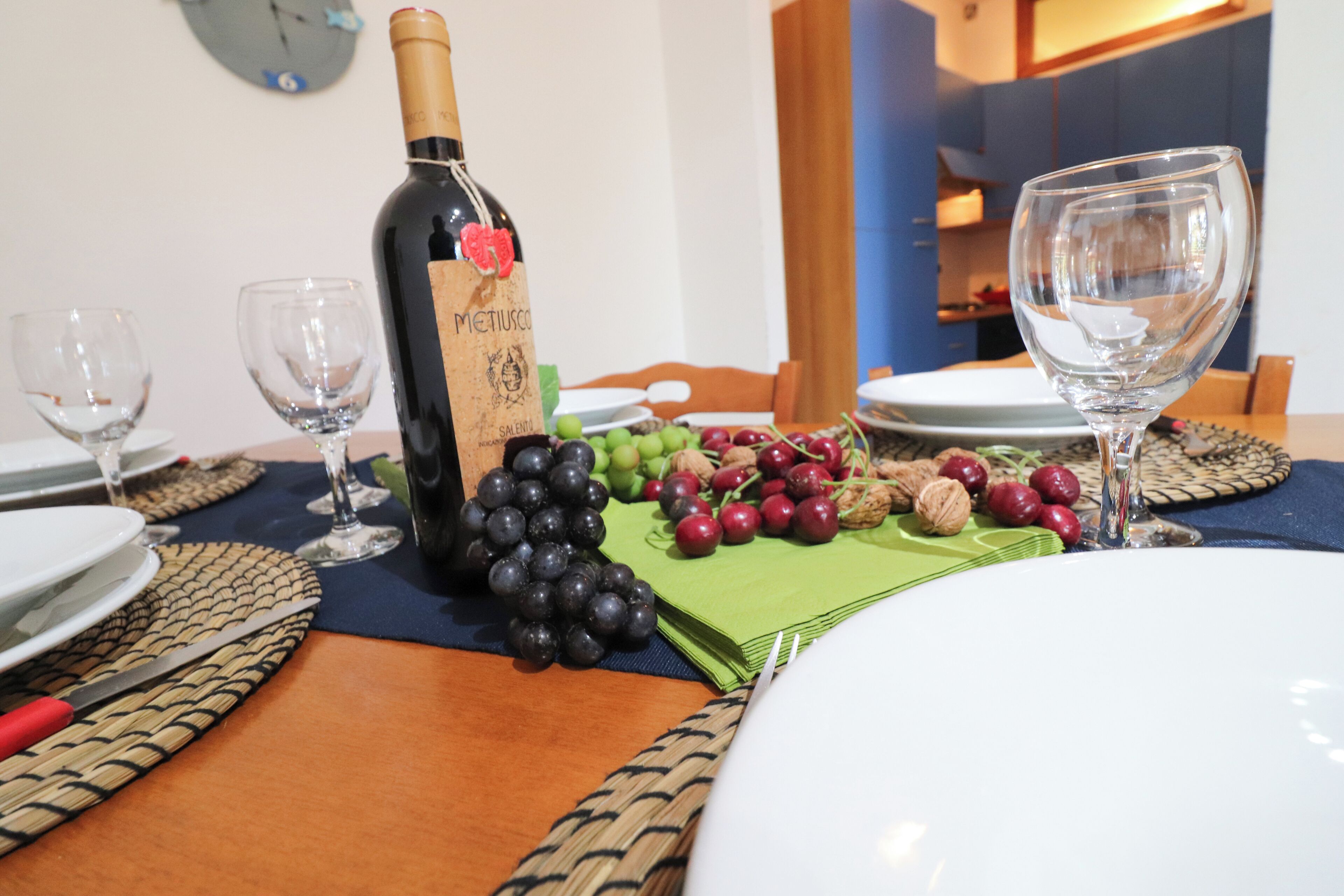 Una mesa de comedor dispuesta con platos, copas de vino, una botella de vino y una variedad de frutas.