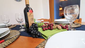 Una mesa de comedor dispuesta con platos, copas de vino, una botella de vino y una variedad de frutas.
