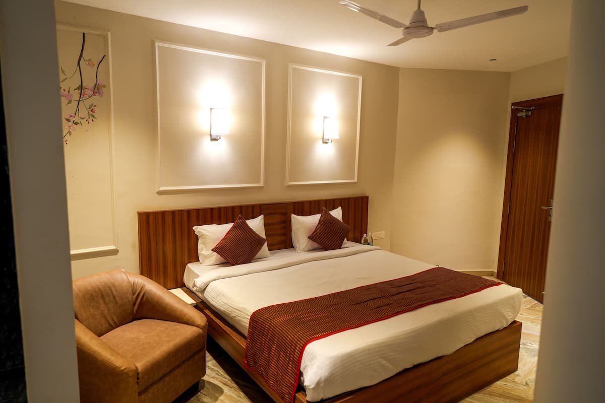 A hotel room with a large bed, a wooden headboard, two wall-mounted lights, a ceiling fan, and a brown leather chair.