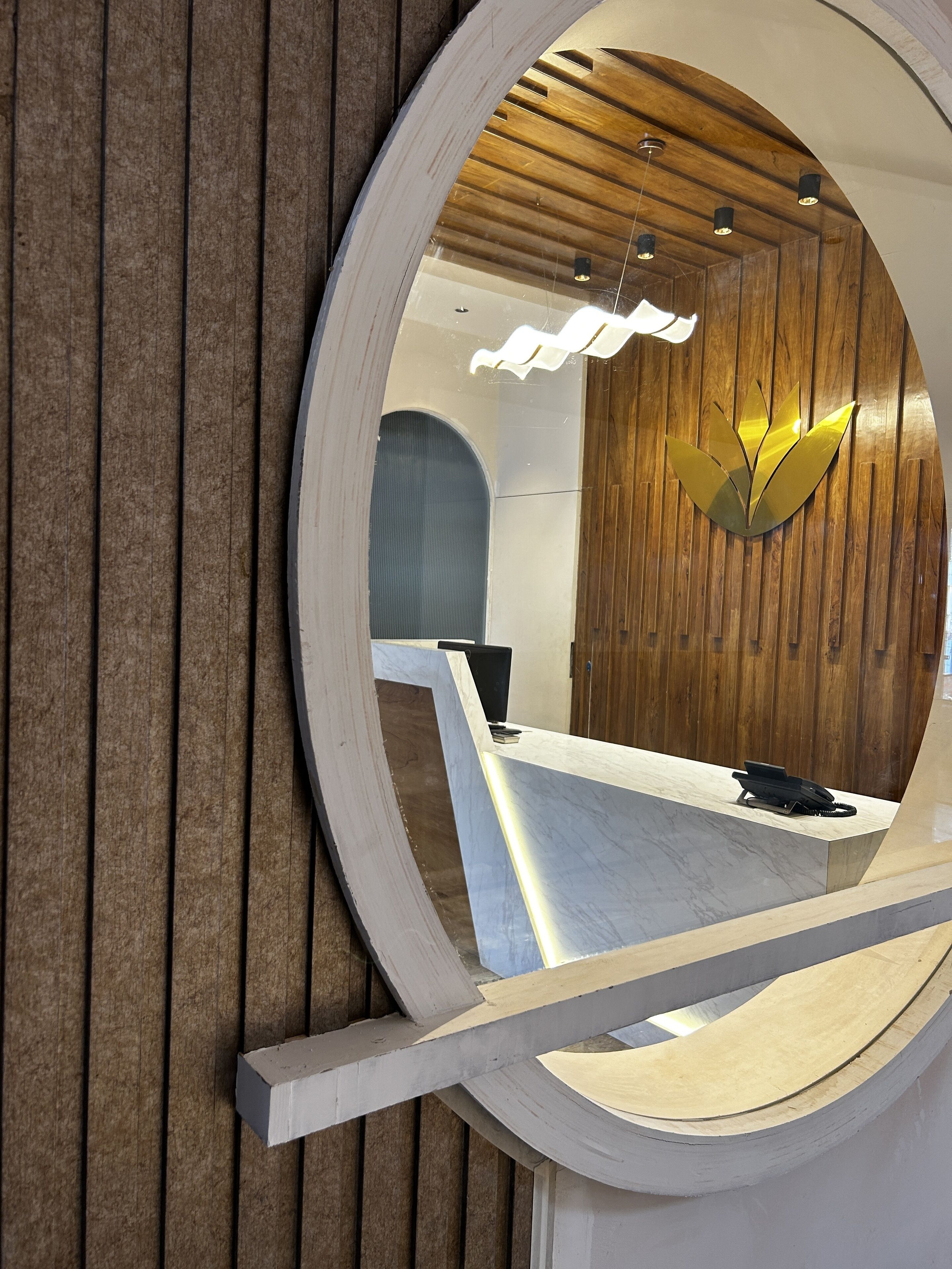 A circular mirror reflecting a modern interior with a wooden wall and a reception desk.