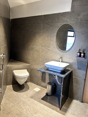 A modern bathroom with a white toilet, a rectangular sink on a black countertop, a round mirror, and a shower area.