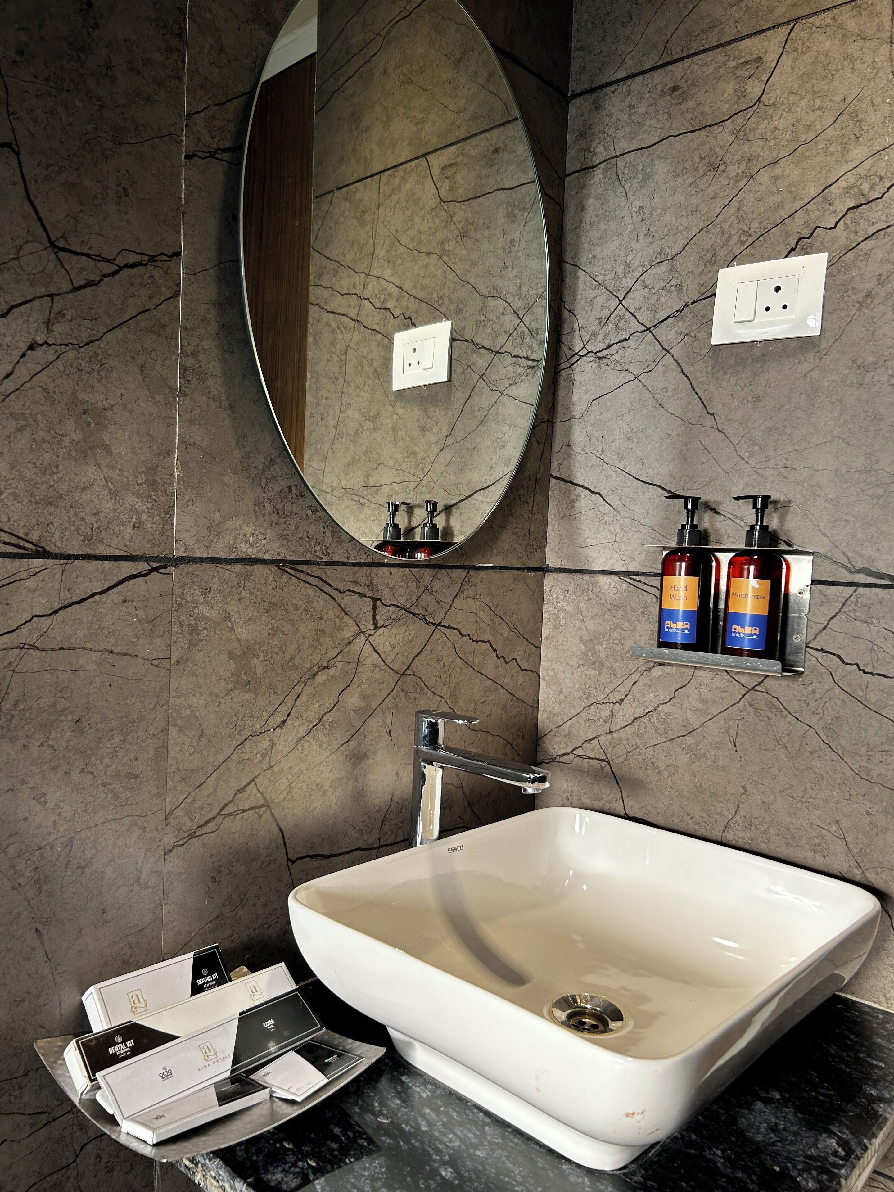 A bathroom with a large oval mirror, a white sink, and toiletries on a shelf.