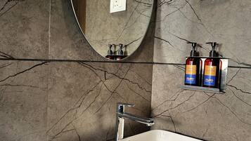 A bathroom with a large oval mirror, a white sink, and toiletries on a shelf.