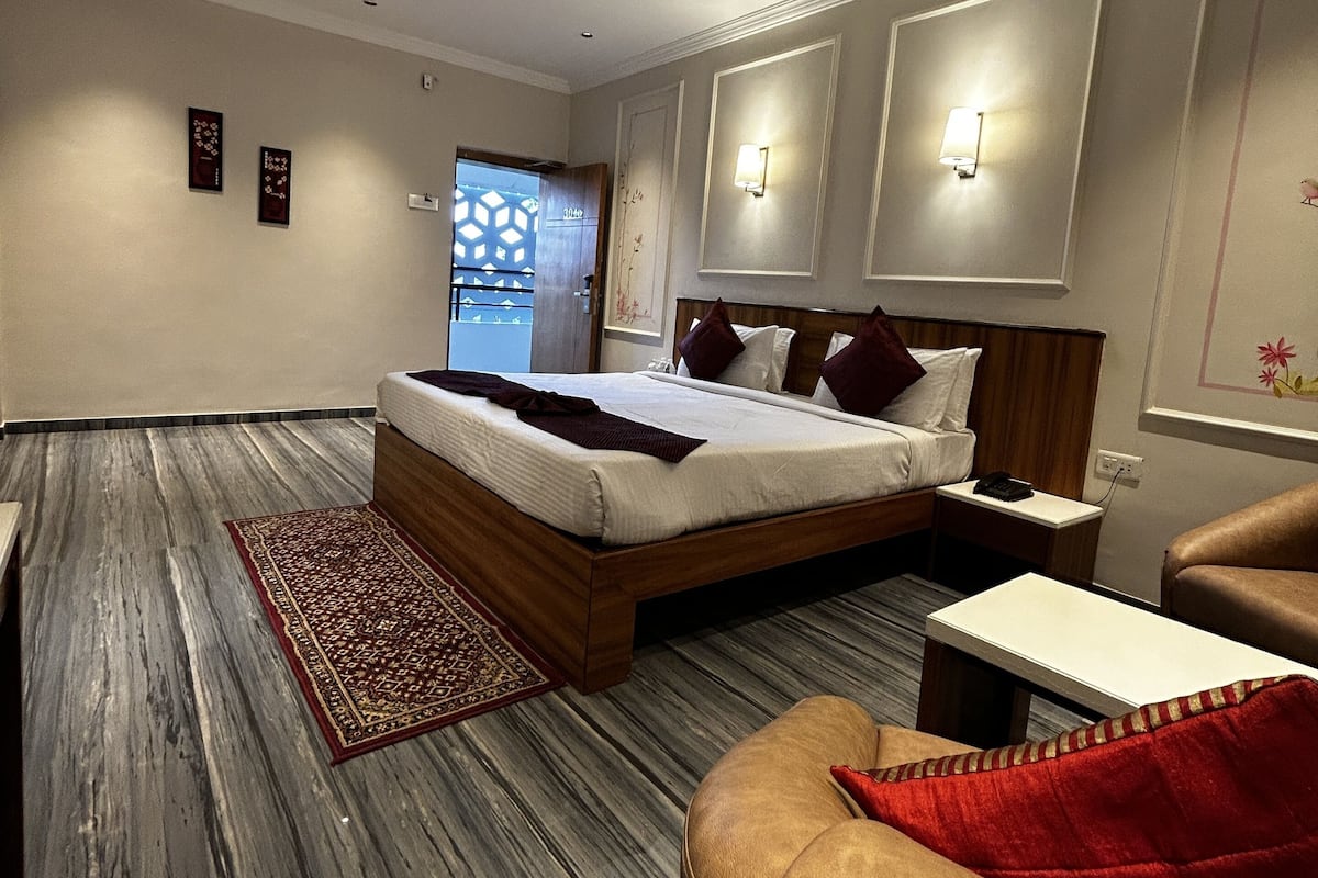 A modern hotel room with a large bed, a ceiling fan, a wooden floor, and a view of the outside.