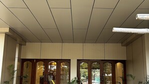 Une entrée d’immeuble avec un plafond carrelé, de grandes portes en bois dotées de panneaux de verre et des plantes en pot.