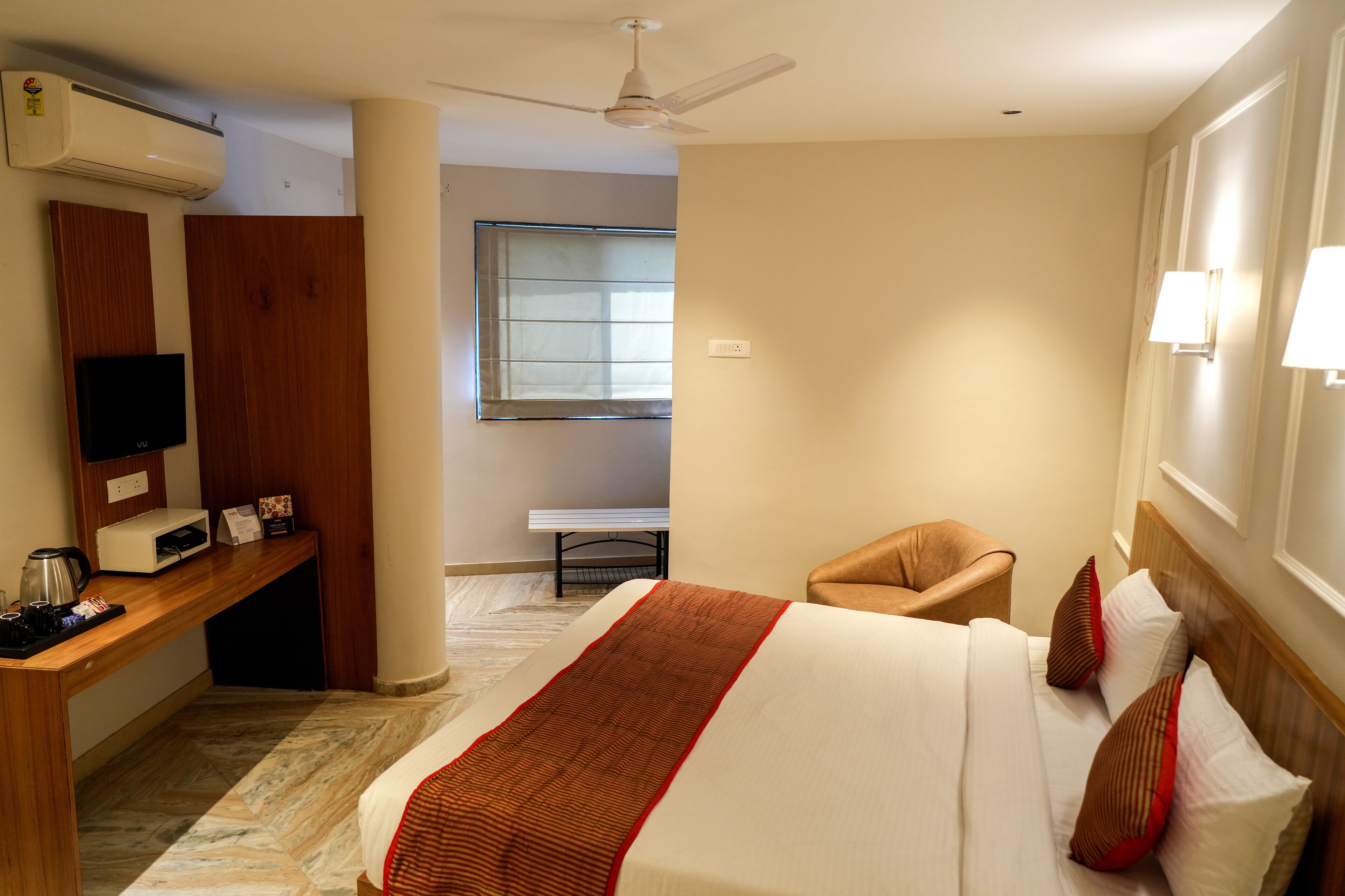 Una habitación de hotel con una cama, un escritorio con computadora, una silla y un ventilador de techo.