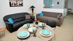 A living room with two sofas, a dining table set with plates and glasses, and a painting on the wall.