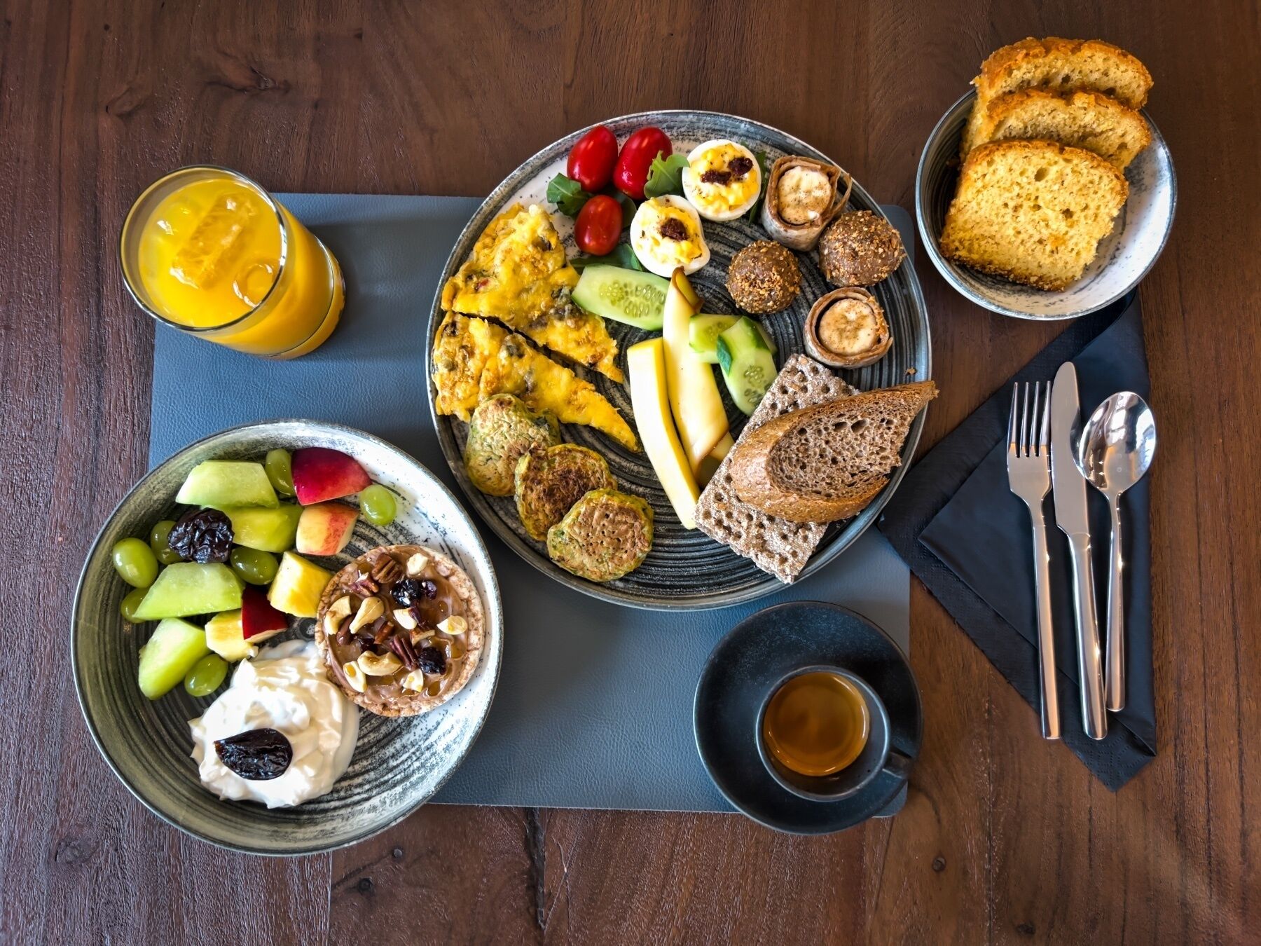A breakfast setting with a variety of foods including toast, eggs, fruit, and a glass of orange juice.