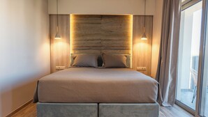 Une chambre moderne avec un grand lit, une tête de lit en bois, des luminaires suspendus et une vue sur l’extérieur.