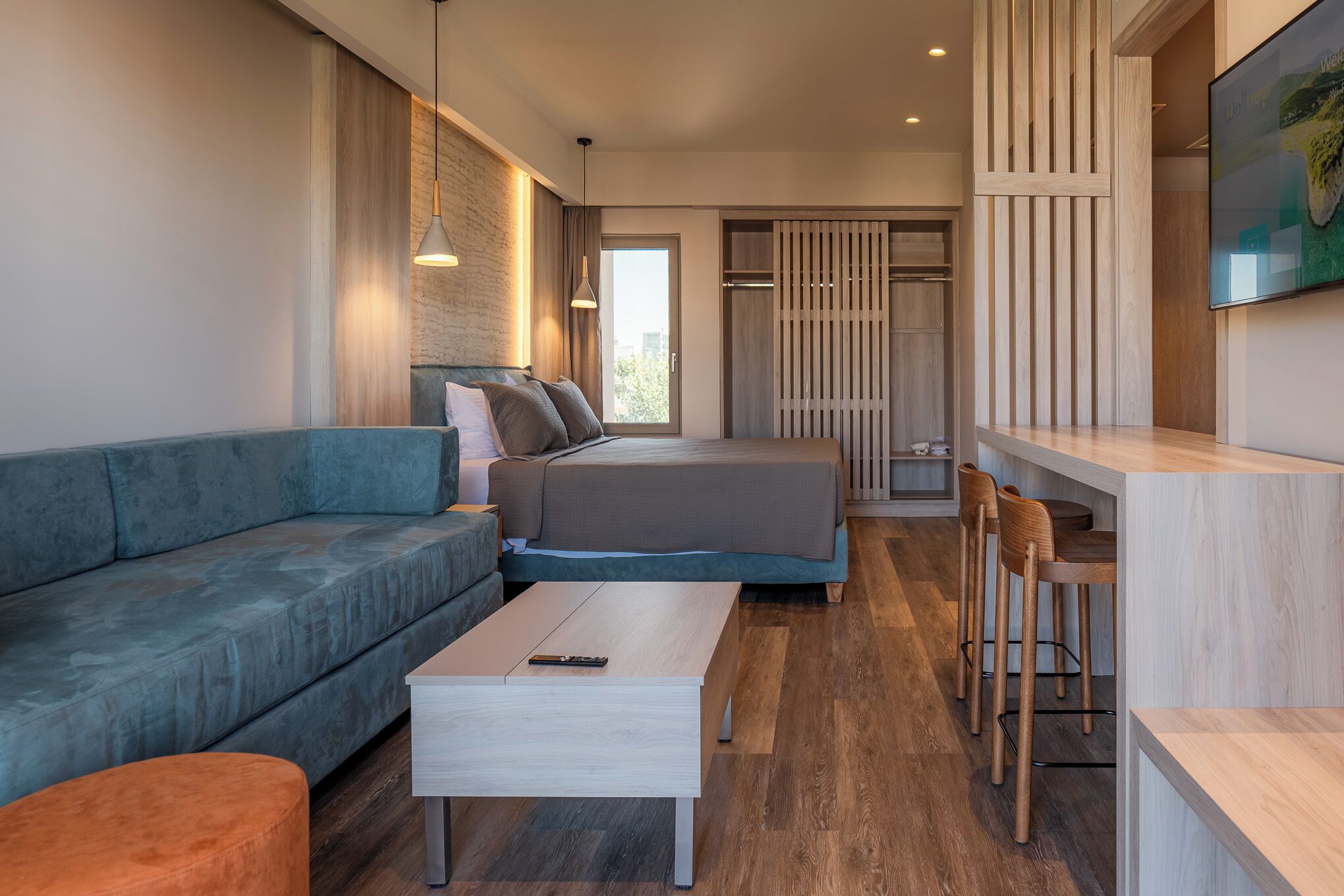 A modern bedroom with a sofa, bed, and a small dining area with stools.