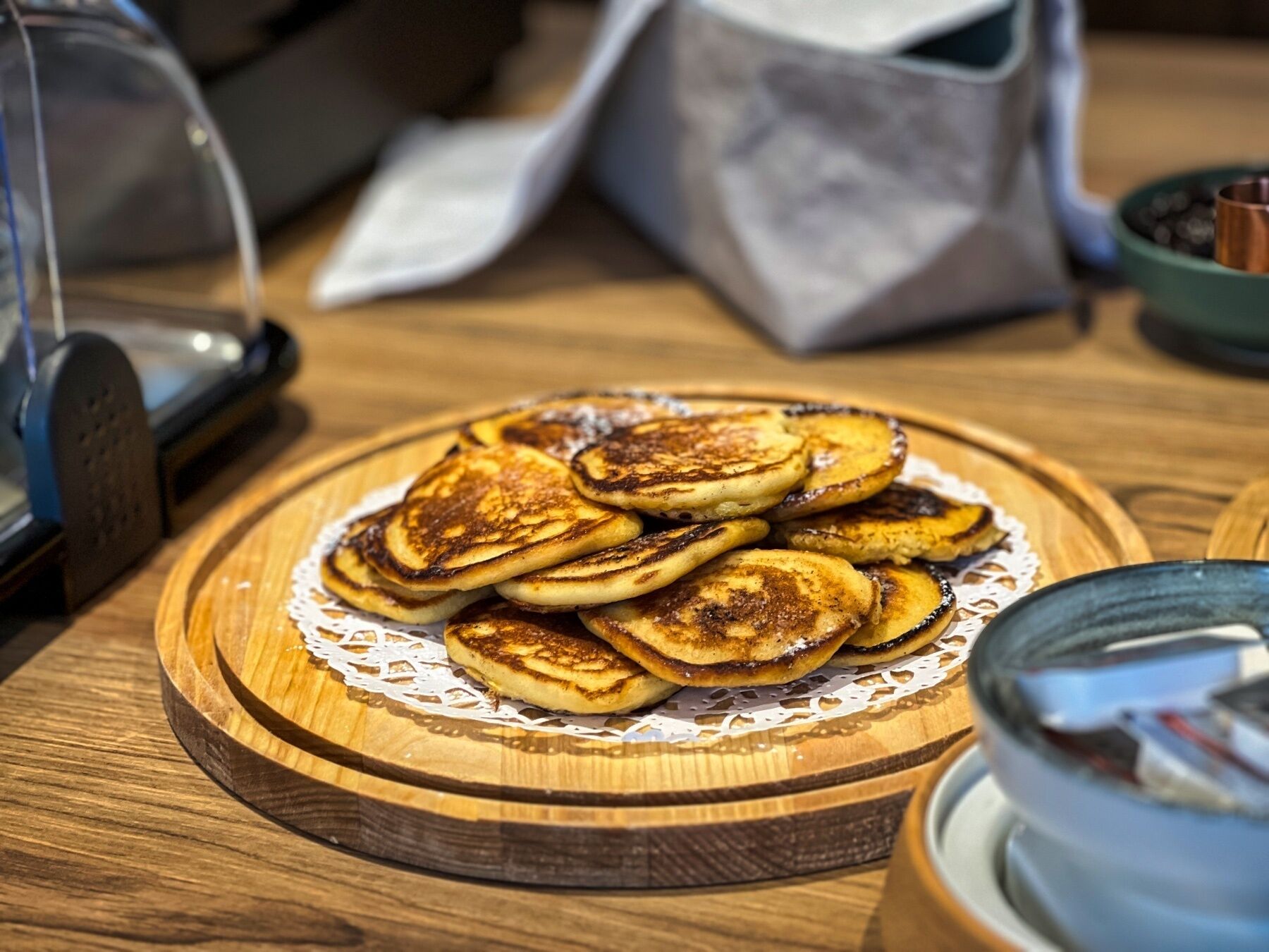 A wooden table with a plate of pancakes, a coffee machine, and a glass of water.