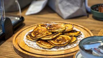 A wooden table with a plate of pancakes, a coffee machine, and a glass of water.