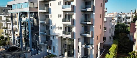 A modern multi-story hotel with balconies, a parking area, and a well-maintained garden.