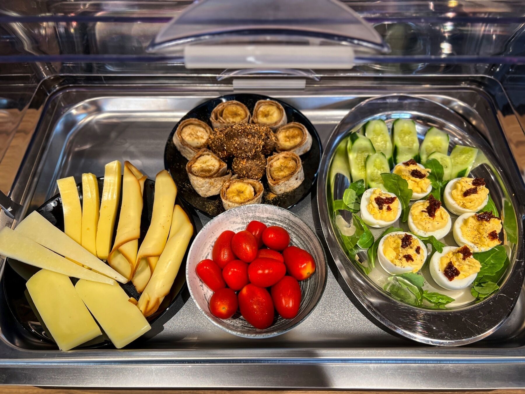 A buffet tray with cheese slices, cherry tomatoes, rolled bananas, and deviled eggs.