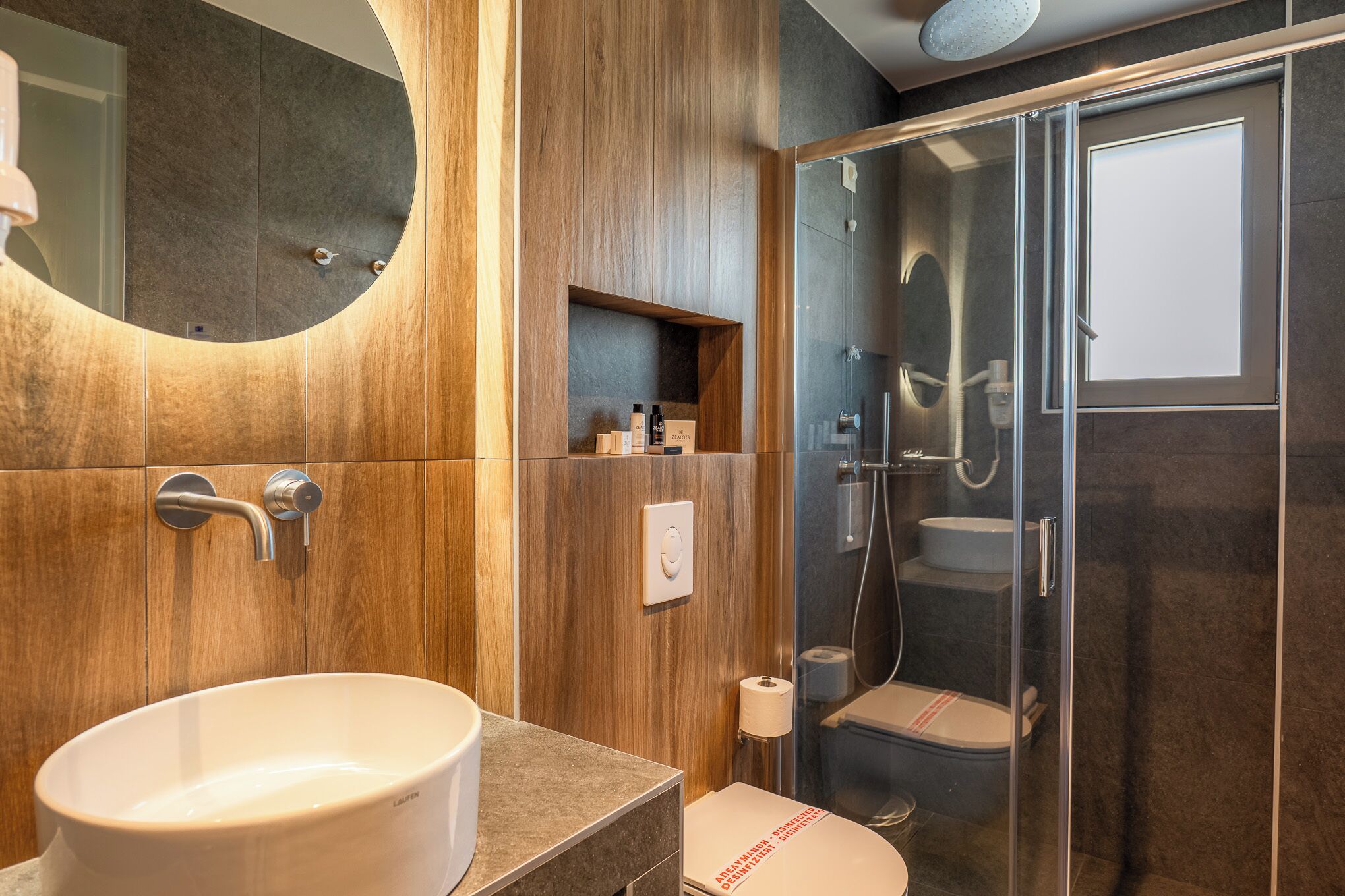A modern bathroom with a large oval sink, a glass-enclosed shower, and a toilet with a red stripe.