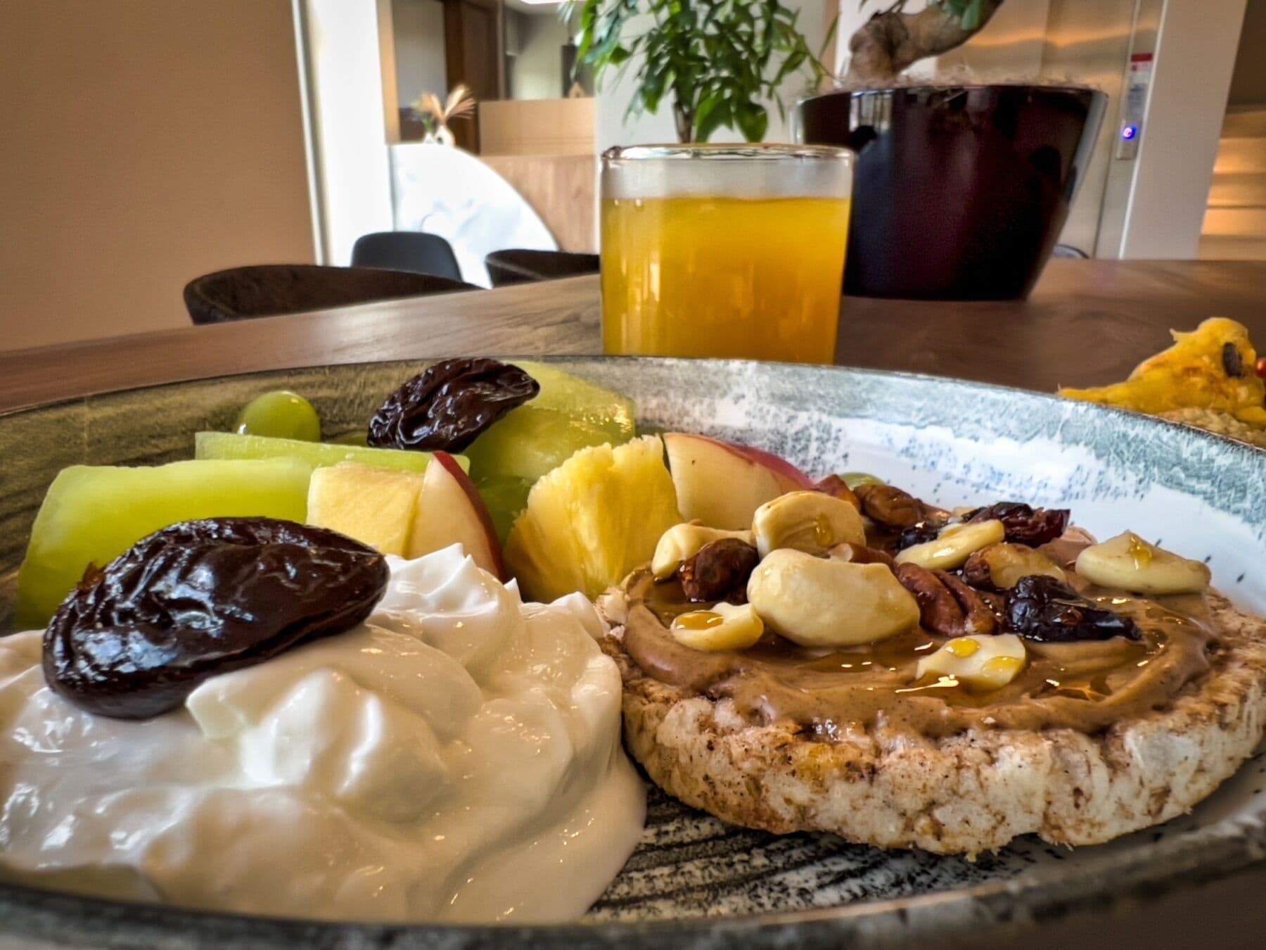 A plate with a slice of grilled chicken topped with peanut butter and nuts, a dollop of yogurt, and sliced fruits including apples and grapes.