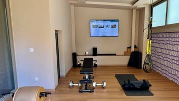 Uma academia moderna em casa, com equipamentos de ginástica, uma TV exibindo um programa de fitness e uma janela grande.