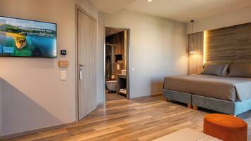 Una habitación de hotel moderna con una cama grande, suelo de madera, un televisor en la pared y un baño visible a través de una puerta abierta.