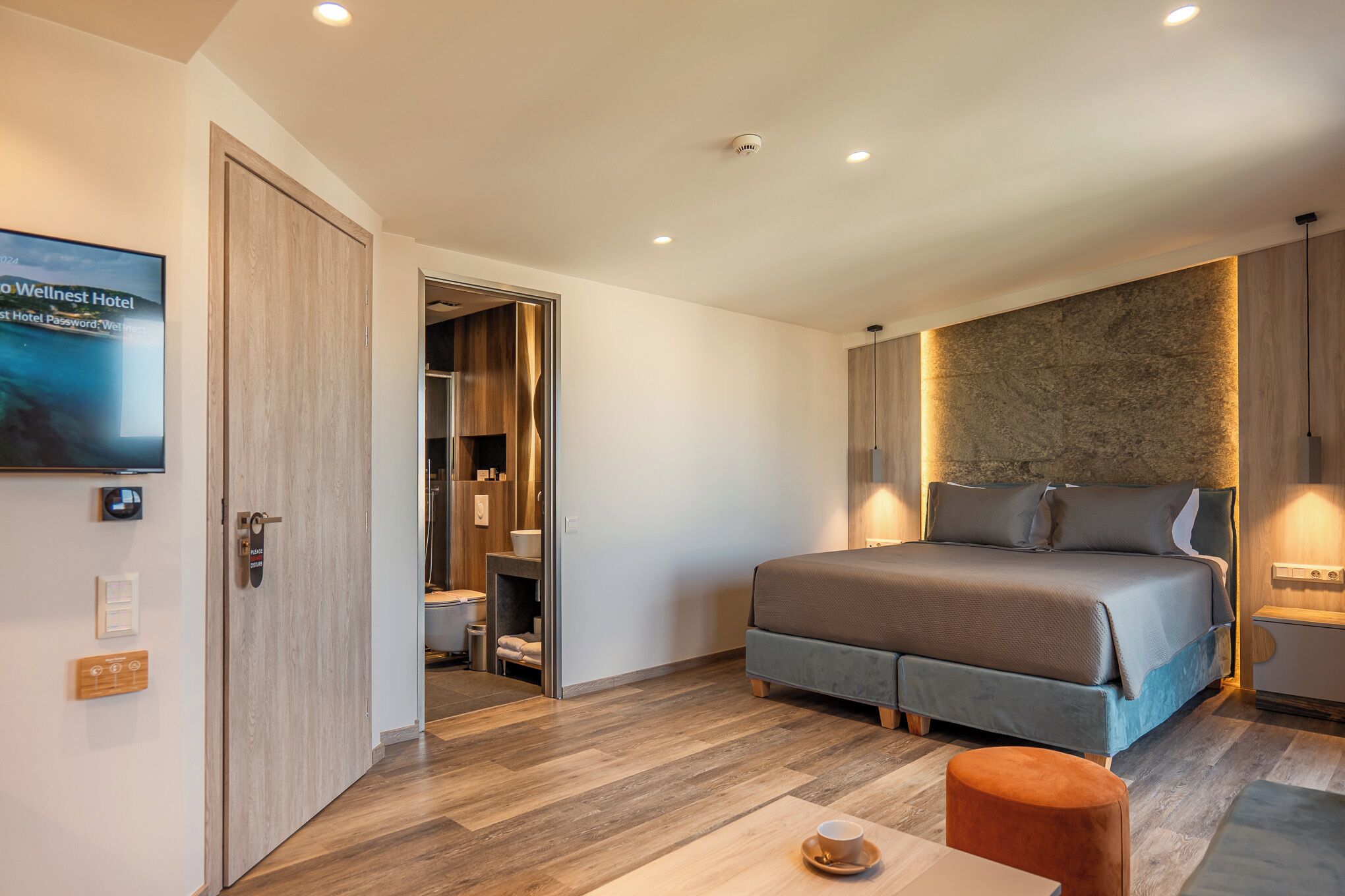 A modern hotel room with a large bed, a wooden wardrobe, a television, and a small table with a cup.