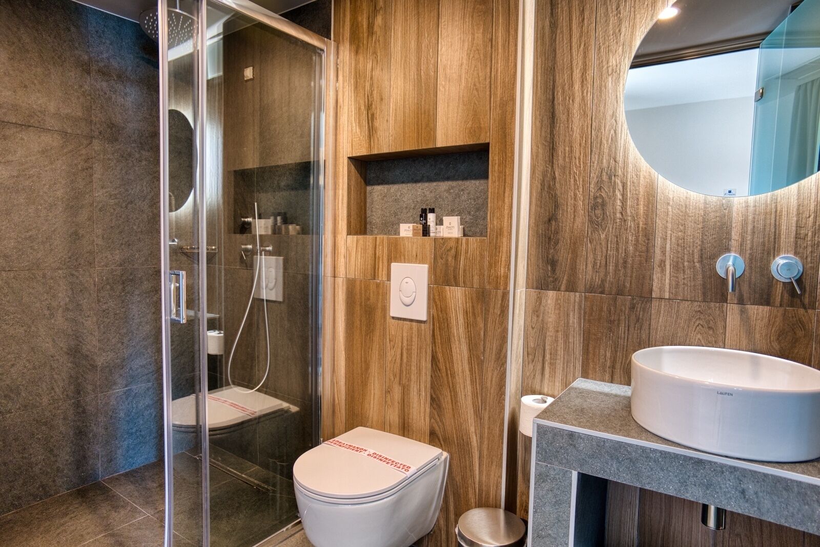 Ein modernes Badezimmer mit einer gläsernen Duschkabine, einer weißen Toilette und einem großzügigen Waschbecken mit Spiegel darüber.
