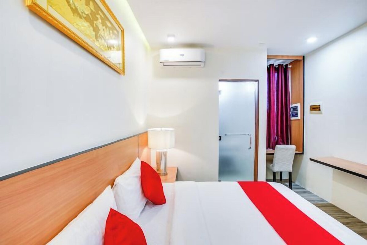 Habitación de hotel con una cama, una mesita de noche con lámpara, una puerta que da a un baño y un escritorio pequeño con silla.