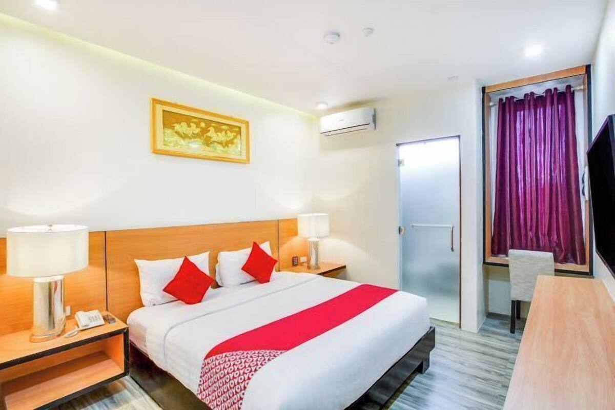 Habitación de hotel con cama, mesitas de noche, televisor, puerta y ventana con cortinas.