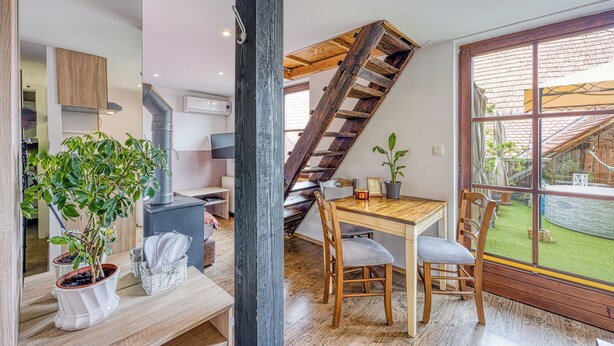 A modern kitchen with a wooden staircase, a dining area with a table and chairs, and a large window overlooking a garden.