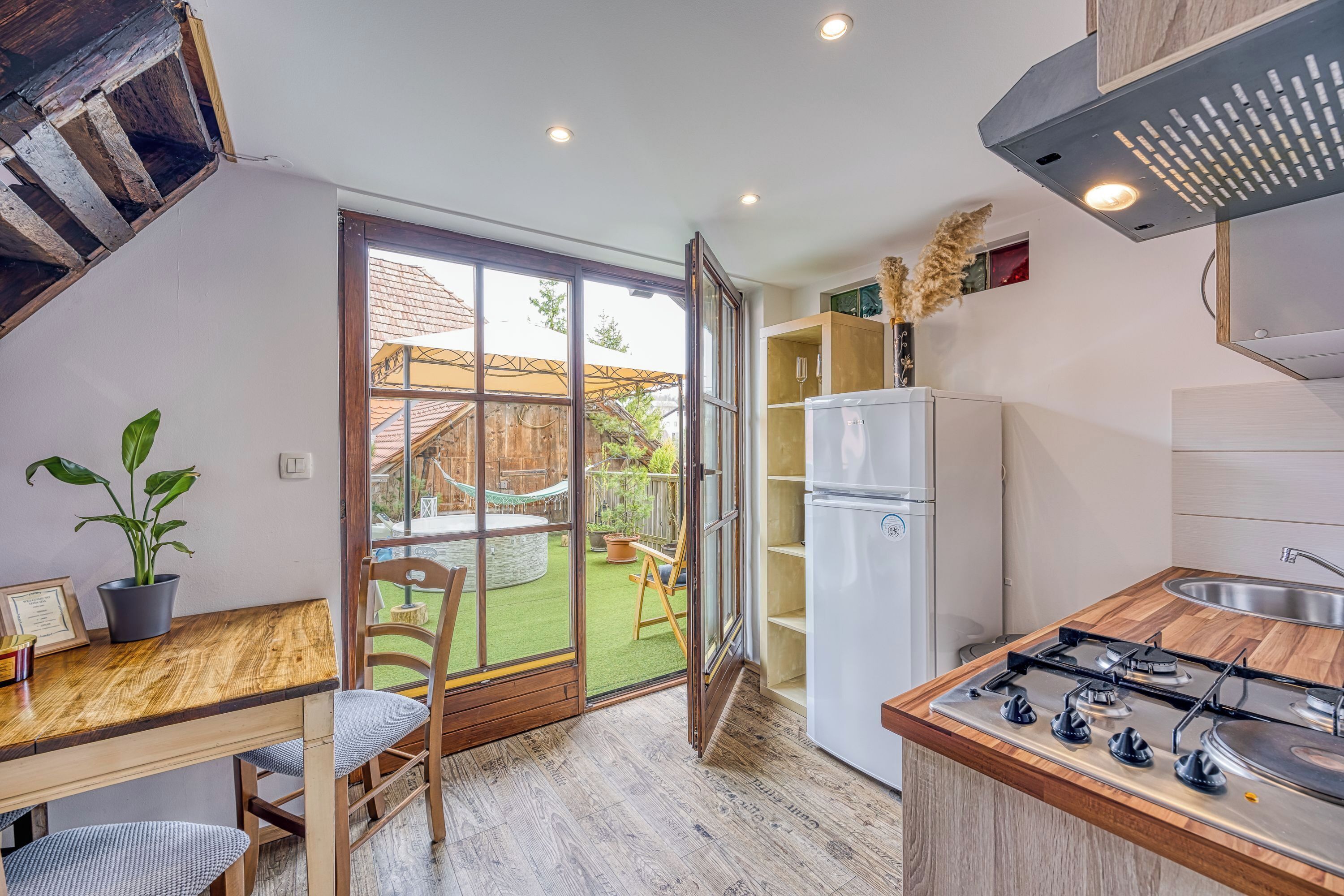 A compact kitchen with a wooden countertop, a gas stove, a refrigerator, and a sliding glass door leading to a patio with a hammock and greenery.