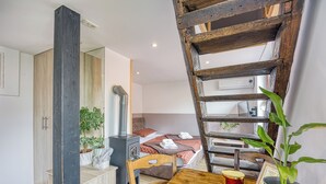 A cozy room with a wooden table, a chair, a potted plant, a ladder, and a bed with a red polka dot blanket.