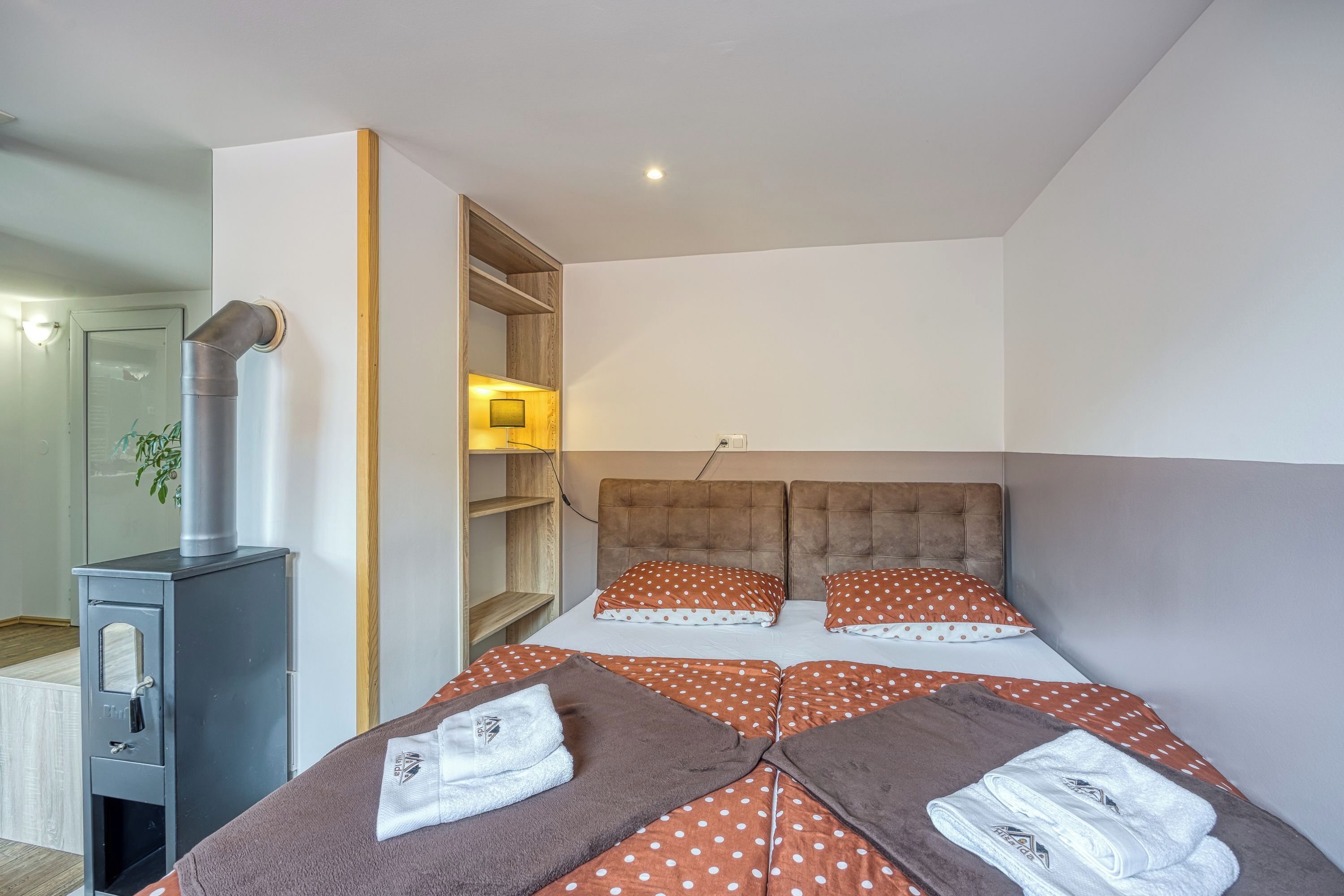 A bedroom with a bed, a wooden wardrobe, a heater, and a shelf unit.