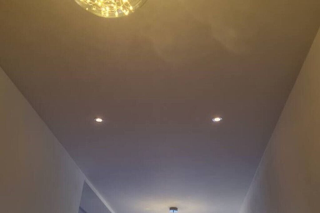 A ceiling with recessed lighting and a central chandelier.