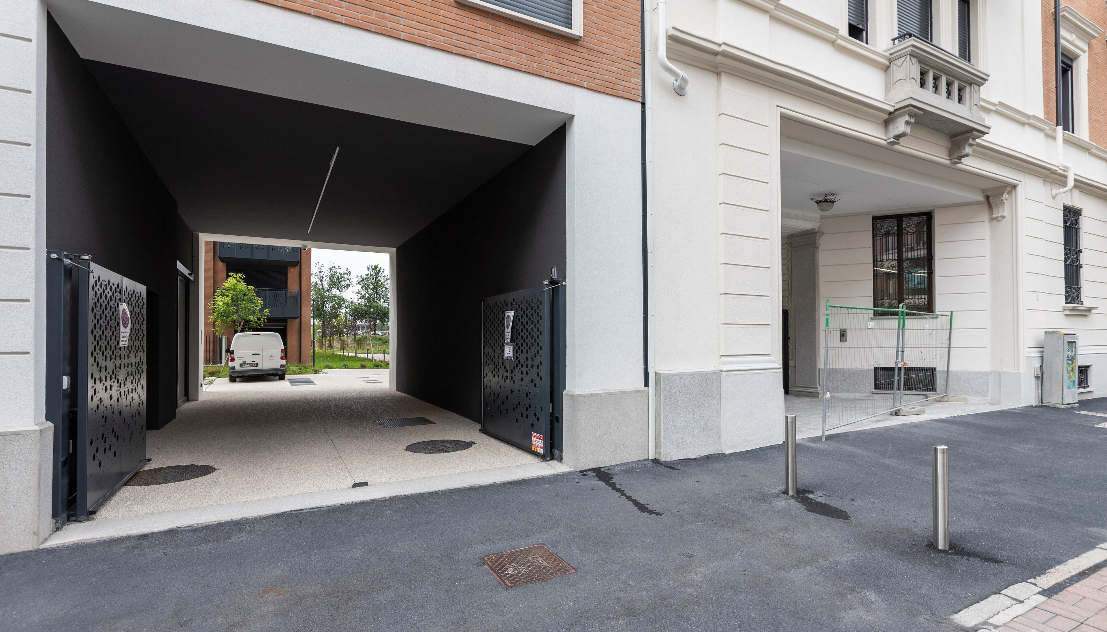 Un área de estacionamiento techada con una camioneta blanca en su interior, una entrada con portón y un edificio con fachada blanca y ventanas negras.