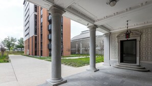 Ein Gebäude mit überdachter Eingangspartie, Säulen und einem Garten.