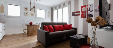 A modern living room with a sofa, a dining table, and a kitchen area.